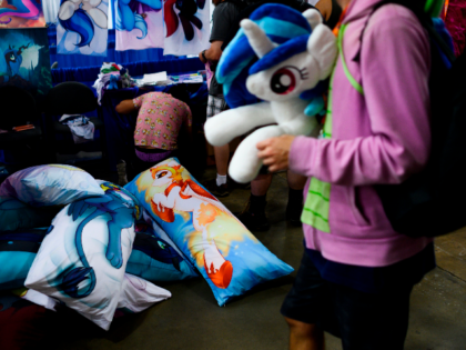An attendee walks past a vendor selling pillows during the BronyCon convention, a gatherin