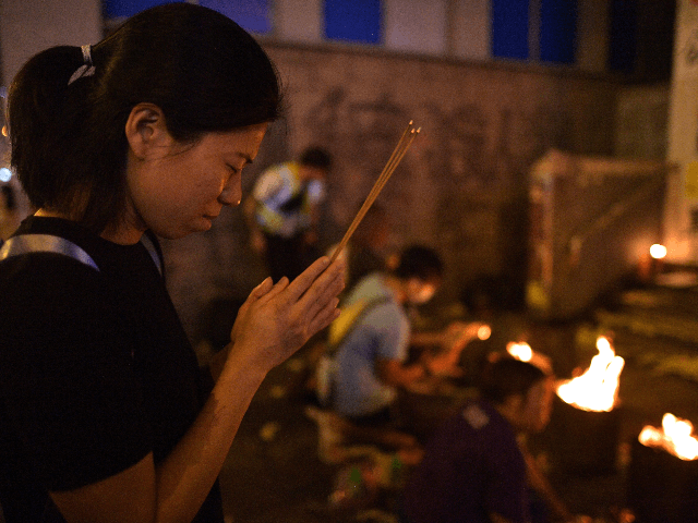A woman holding insense prays at a makeshift shrine outside the Mongkok district police st