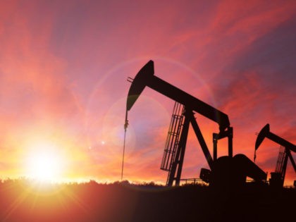 Pump jack silhouette against a sunset sky with deliberate lens flare and copy space. These