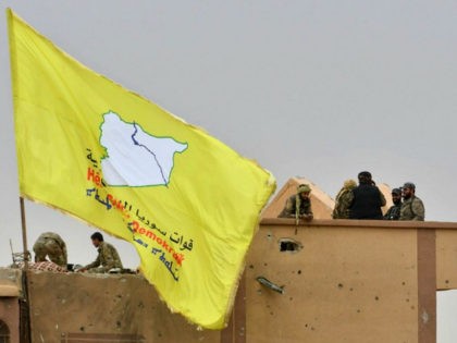 Fighters of the Syrian Democratic Forces (SDF) stand atop a roof next to their unfurled fl