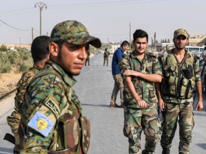 A fighter (L) wearing a military uniform bearing the insignia of the Manbij Military Council (MMC), affiliated with the Syrian Democratic Forces (SDF) Kurdish-led alliance, stands by as Syrian government soldiers walk past at a position on the outskirts of the northern city of Manbij in the north of Aleppo …
