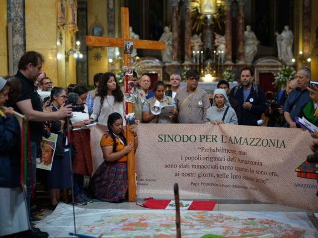 People pray and hold banner in Santa Maria in Transpontina Church, during a Via Crucis (Way of the Cross) procession of members of Amazon indigenous populations from St. Angelo Castle to the Vatican, Saturday Oct. 19, 2019. Pope Francis is holding a three-week meeting on preserving the rainforest and ministering …
