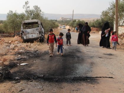 Syrians walk past a damaged van at the site of helicopter gunfire which reportedly killed