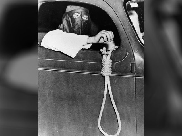 A hangman's noose dangling from an automobile driven by a hooded Ku Klux Klan member