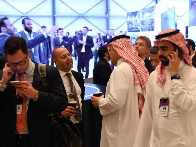 Delegates chat during the Future Investment Initiative (FII) forum at the King Abdulaziz Conference Centre in Saudi Arabia's capital Riyadh, on October 29, 2019, in front of a screen transmitting images of Saudi Crown Prince Mohammed bin Salman visiting an exhibition. - Top finance moguls and political leaders were expected …