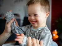 Cute boy with Down syndrome playing with dad on in home living room