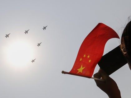 A woman holding a Chinese national flag films Chinese military planes fly in formation pas