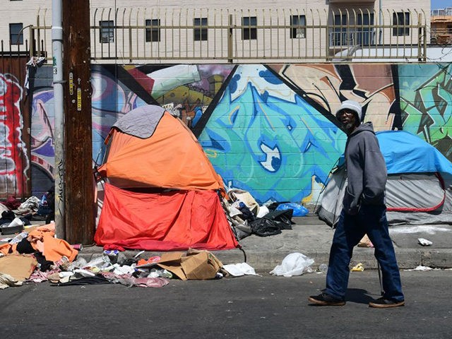 A pedestrian walks past tents and trash on a sidewalk in downtown Los Angeles on May 30, 2019. - The city of Los Angeles on May 29 agreed to allow homeless people on Skid Row to keep their property and not have it seized, providing the items are not bulky …
