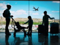 mother with kids and luggage looking at planes in airport, family travel
