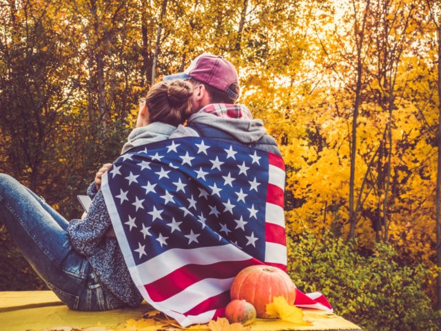 Happy married couple holding the US flag against the background of yellow trees and the se