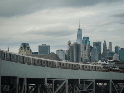 With Lower Manhattan and One World Trade Center standing behind it, a subway train moves a