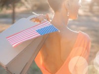 Young woman holding American flag and paper bag in spring park