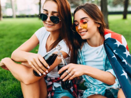 Two attractive young girls in sunglasses sitting in the Park on the lawn with the American