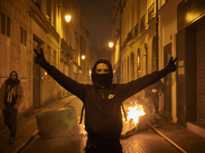 PARIS, FRANCE - NOVEMBER 16: A Black Bloc protestor celebrates next to a burning barricade as protests to mark the Anniversary of the Gilets Jaune movement turn violent in Paris as thousands of protesters converged on the French capital on November 16, 2019 in Paris, France. One of the most …