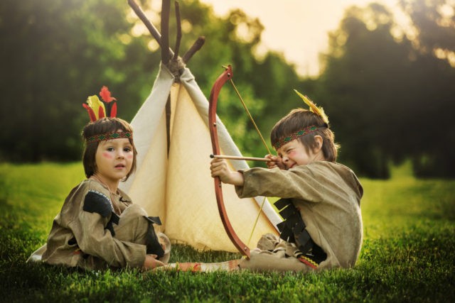 Cute portrait of native american boys with costumes, playing outdoor in the park with bow,