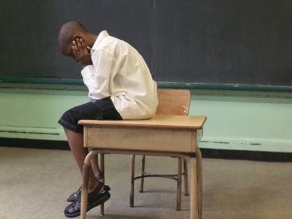 Boy sitting on top of desk by blackboard