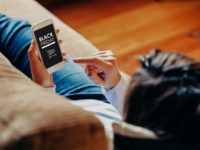 Black Friday banner in a mobile phone that is in the hand of woman at home.