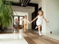 Happy young family with cardboard boxes in new home at moving day concept, excited children running into big modern own house hallway, parents with belongings at background, mortgage loan, relocation