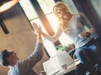 Handsome young man and attractive young woman are spending time together. Romantic couple is working in cafe and giving five.