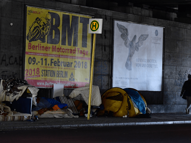 People walk past tents at a makeshift homeless encampment under a bridge on March 1, 2018