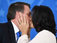 Brazilian President Jair Bolsonaro (L) and First Lady Michelle Bolsonaro kiss during the commemoration ceremony of the National Volunteer Day, at Planalto Palace in Brasilia, on August 28, 2019. - Bolsonaro on Wednesday repeated a demand for French leader Emmanuel Macron to withdraw recent remarks, as he accused France and …
