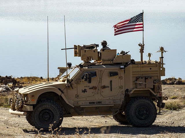 A US soldier sits atop a military vehicle, part of a joint convoy with the Kurdish People'