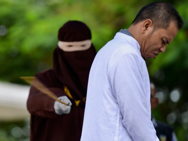 Aceh Ulema Council (MPU) member Mukhlis reacts as he is whipped in public by a member of the Sharia police in Banda Aceh on October 31, 2019. - An Indonesian man working for an organisation which helped draft strict religious laws ordering adulterers to be flogged was himself publically whipped …