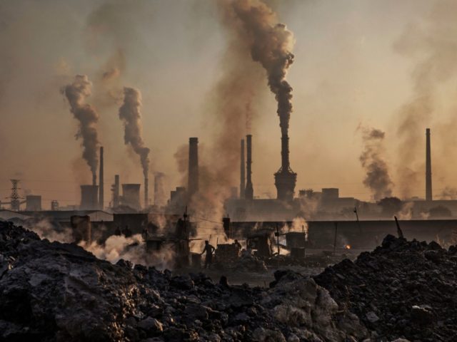 INNER MONGOLIA, CHINA - NOVEMBER 04: Smoke billows from a large steel plant as a Chinese labourer works at an unauthorized steel factory, foreground, on November 4, 2016 in Inner Mongolia, China. To meet China's targets to slash emissions of carbon dioxide, authorities are pushing to shut down privately owned …