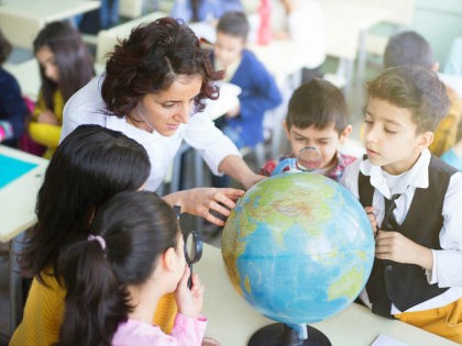 female teacher and students looking the globe with a magnifying glass in the classroom