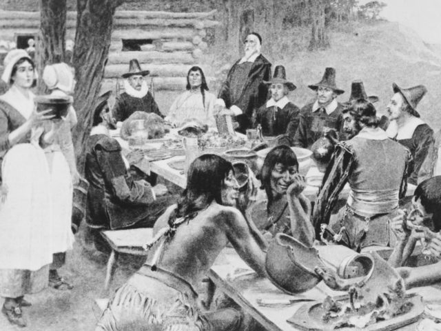 A depiction of early settlers of the Plymouth Colony sharing a harvest Thanksgiving meal with members of the local Wampanoag tribe at the Plymouth Plantation, Plymouth, Massachusetts, 1621. (Photo by Frederic Lewis/Archive Photos/Getty Images)