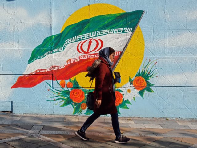 An Iranian woman walks past a mural painting of the Islamic republic's national flag in ce