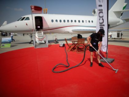 DUBAI, UNITED ARAB EMIRATES - NOVEMBER 18: A woman vacuum cleans the red carpet next a private jet display during the Dubai Airshow on November 18, 2013 in Dubai, United Arab Emirates. The Dubai Air Show is the premier Middle East air show for trade and business delegates organized by …