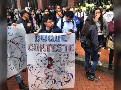 A left-wing protester holds up a sign reading "Duque, answer," with a baby representing Colombian President Ivan Duque answering the phone. The image is part of widespread protests in Colombia on November 21,2019.