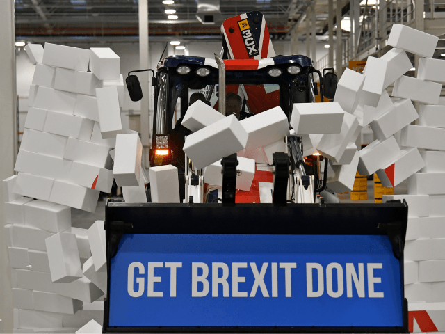 TOPSHOT - Britain's Prime Minister and Conservative party leader Boris Johnson drives a Union flag-themed JCB, with the words "Get Brexit Done" inside the digger bucket, through a fake wall emblazoned with the word "GRIDLOCK", during a general election campaign event at JCB construction company in Uttoxeter, Staffordshire, on December …