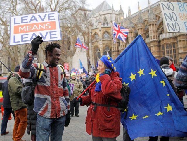 A pro-Brexit activist (L) holding a placard and wearing a union flag-themed shirt talks wi