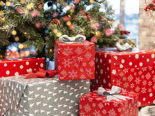 Gift boxes under Christmas tree, New Year home decorations, red wrapping Santa presents, fir tree decorated, beautiful bokeh of garland. Living room with fireplace decorated for Christmas holiday.