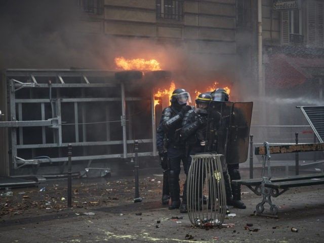 PARIS, FRANCE - DECEMBER 05: Police guard a burning caravan as demonstrations turn violent during a rally near Place de Republique in support of the national strike in France, one of the largest nationwide strikes in years, on December 05, 2019 in Paris, France. President Emmanuel Macron is facing his …