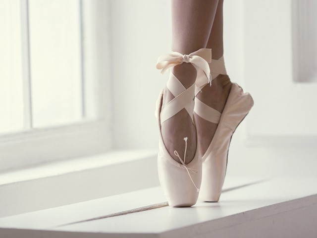 Legs of a ballerina in pink pointe shoes with a bow are dancing near the window