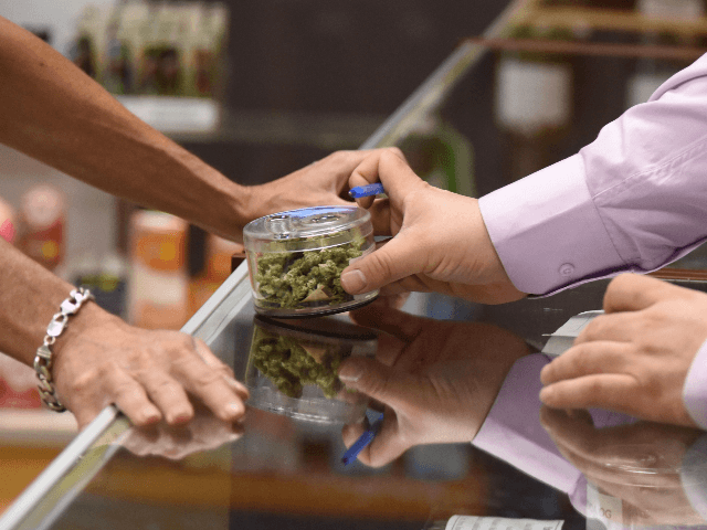 A budtender (right) shows cannabis buds to a customer at the Green Pearl Organics dispensary on the first day of legal recreational marijuana sales in California, January 1, 2018 at the Green Pearl Organics marijuana dispensary in Desert Hot Springs, California. / AFP PHOTO / Robyn Beck (Photo credit should read ROBYN BECK/AFP via Getty Images)