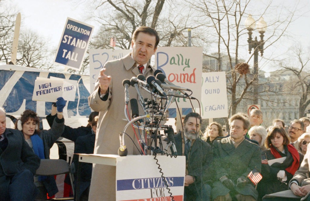 White House Communications Director Patrick Buchanan speaks at a rally, Monday, Jan. 5, 1987 in Lafayette Park, Washington across from the White House, in support of President Reagan against critics of the Iran-Contra affair. (AP Photo/Dennis Cook)