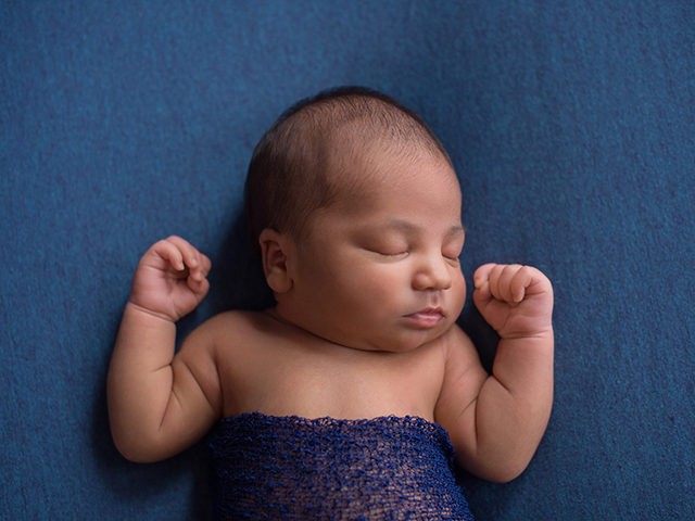 Headshot of a sleeping, nine day old newborn baby boy. Shot in the studio on denim blue material.