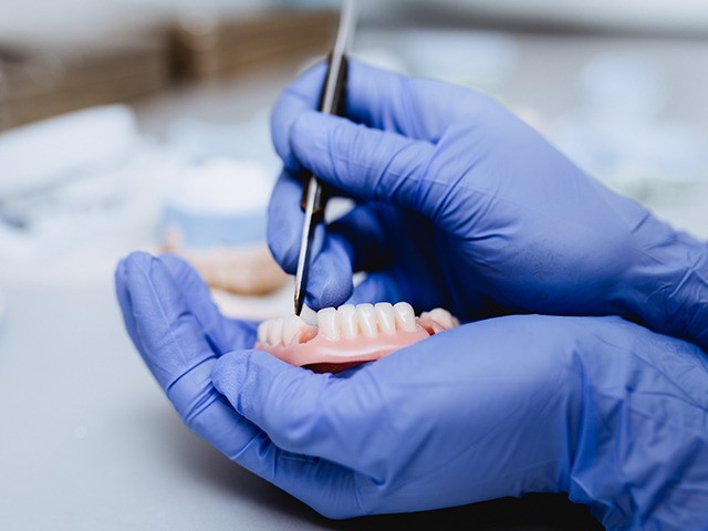 Dental prosthesis, prosthetics work. Close up of prosthetic's hands while working on the d