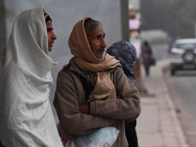 Commuters wrapped in warm clothes wait at a bus stop on a cold foggy morning in New Delhi