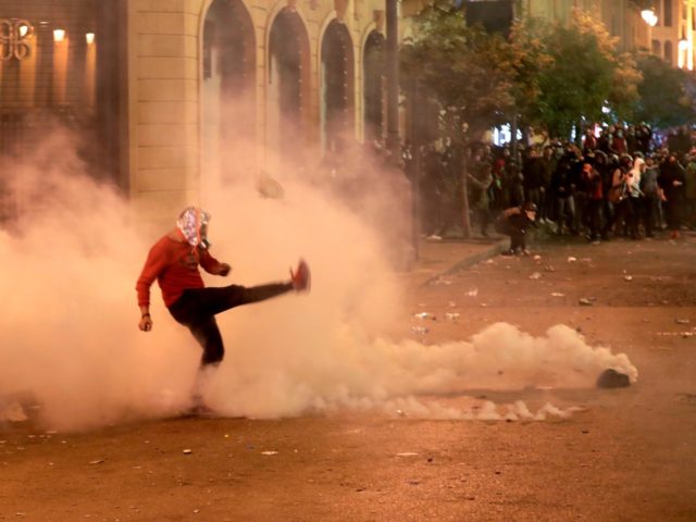 TOPSHOT - A Lebanese demonstrator kicks back a tear-gas canister during clashes with riot