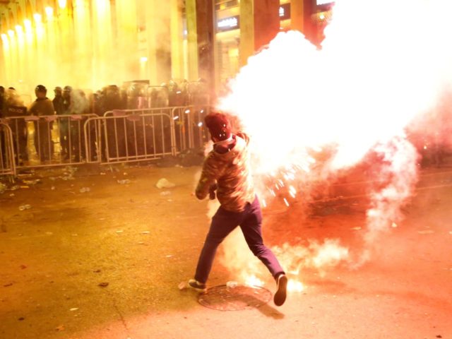 An anti-government protester throws flares against the riot police, background, during a p