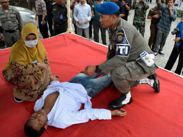 An Indonesian man faints after he was whipped in public on charges of engaging in sexual r
