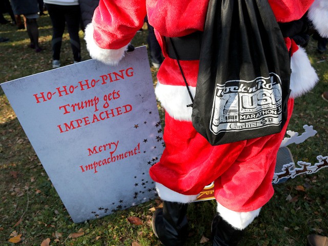 A protester wearing a Santa Claus costume holds a sign during an impeachment rally outside