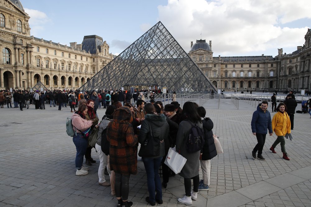 Visitors wait as striking employees demonstrate outside the Louvre museum Friday, Jan. 17, 2020 in Paris. Paris' Louvre museum was closed Friday as dozens of protesters blocked the entrance to denounce the French government's plans to overhaul the pension system. (AP Photo/Francois Mori)