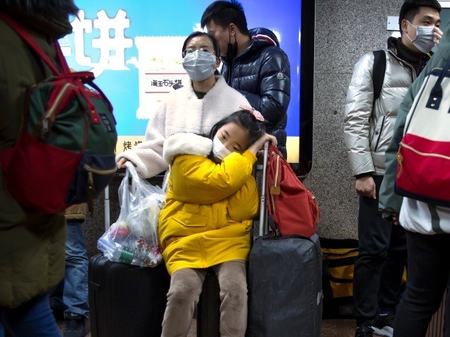 A girl wears a face mask as she sits on a suitcase at the Beijing West Railway Station in