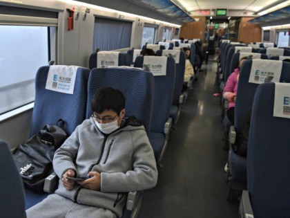 A young man wearing a protective facemask sits on a train usually full with passengers ahe